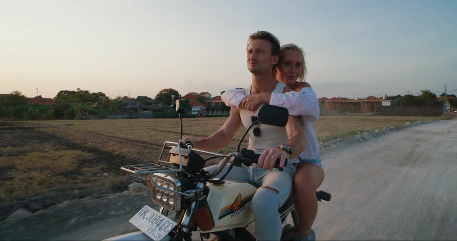 Smiling man driving a motorcycle and a woman behind hugging him affectionately