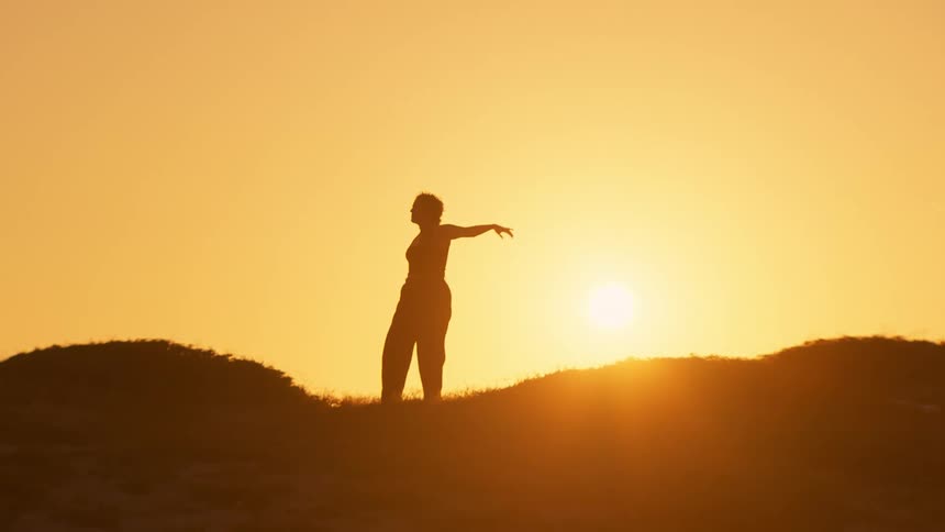 A woman performs stretches while standing on grass on a hilly open area