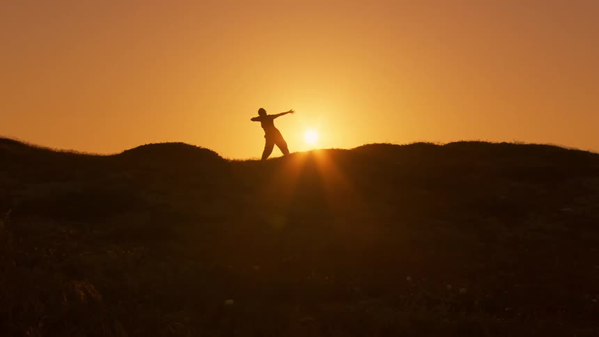 A silhouette of a person doing martial arts movements and behind there is a strong sun and an orange sky