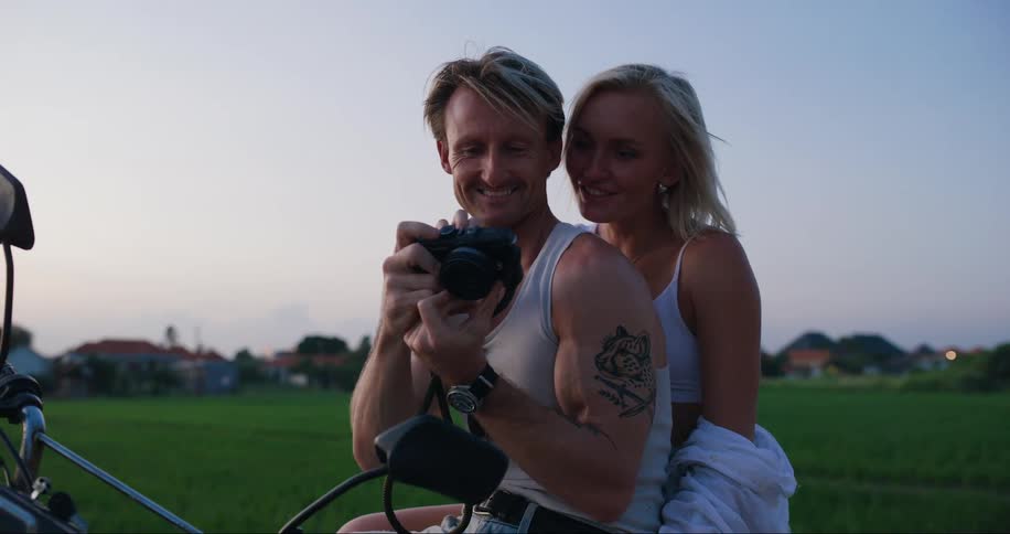 Man and woman sitting on a motorcycle watching and using a camera