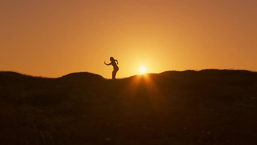 Silhouette of a person making body movements on a hill with the setting sun in the background