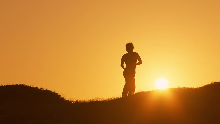 Silhouette of a person on a hill against a golden sun dancing