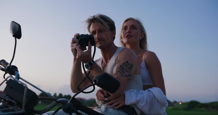 A man and woman sit on a motorcycle taking photos