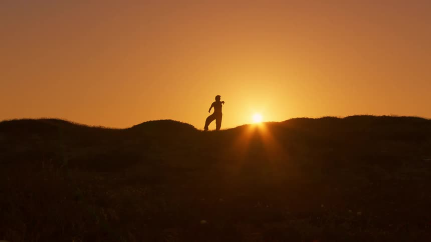 A woman is doing tai chi on the hill at sunrise
