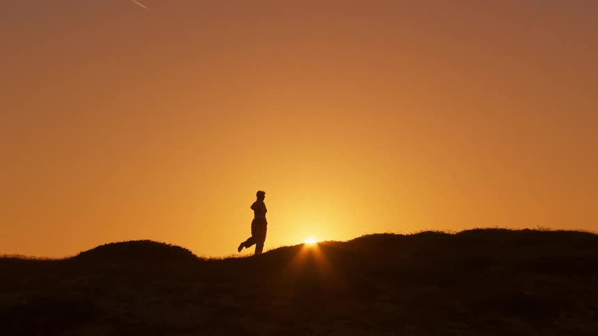 Landscape of a golden sun and the silhouette of a mountain and a person in motion