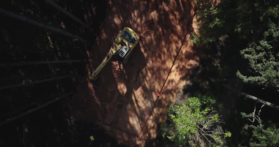 An aerial view of a yellow excavator in a forested area