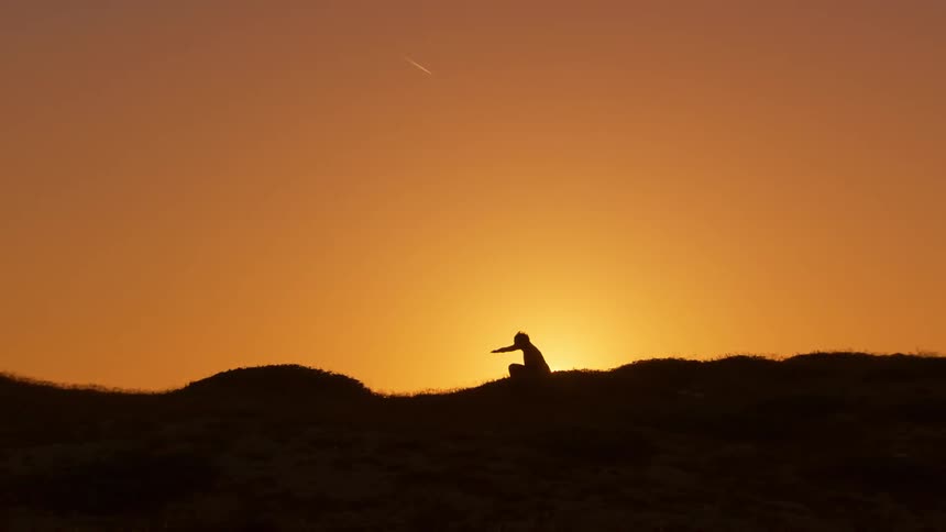Woman moves through various poses while silhouetted against an orange sky