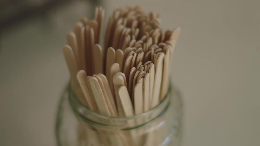 A person drops a bunch of wooden popsicle sticks into a glass jar