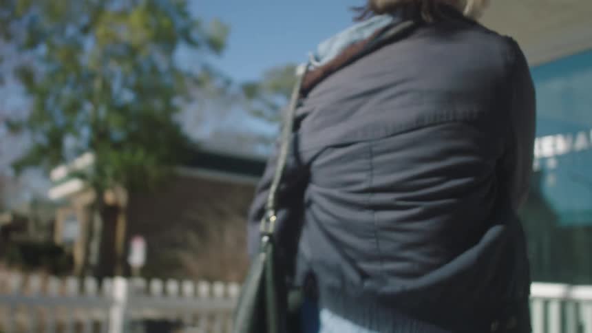 Blonde woman rushes along sidewalk and enters store