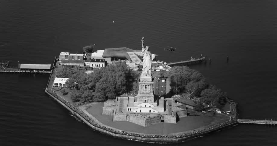 Aerial view of the statue of liberty and its surrounding island with a helicopter passing nearby