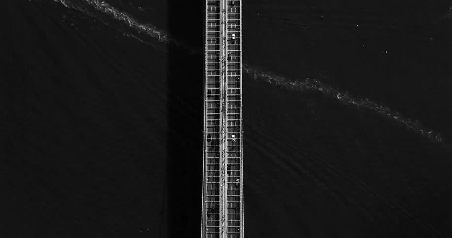 An aerial black and white footage of vehicles driving over a bridge