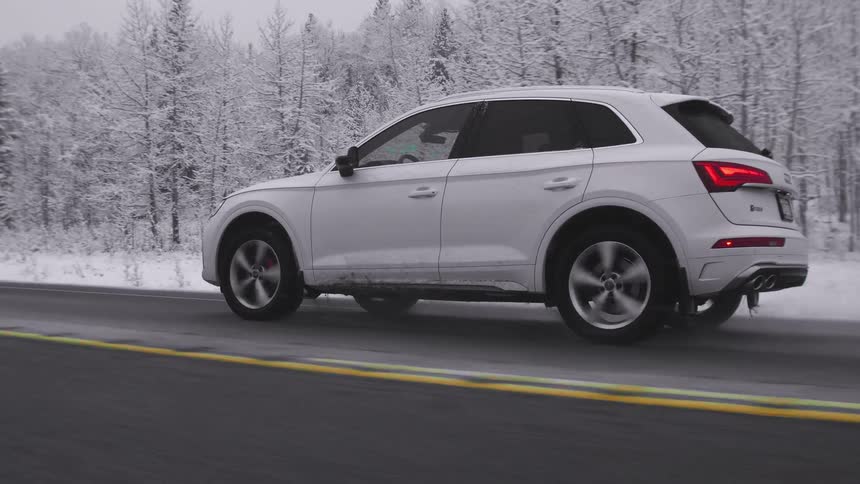 A white four door vehicle driving on a road through a forest in the winter