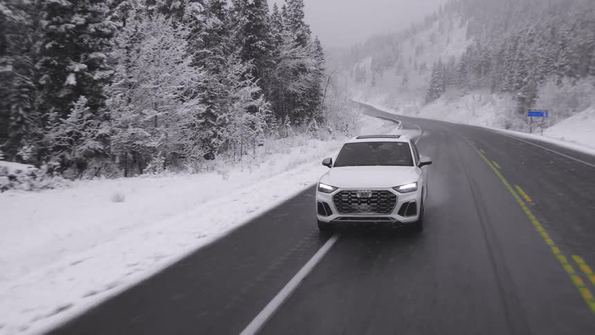 A white sport utility vehicle drives along a road that passes through snow covered forests