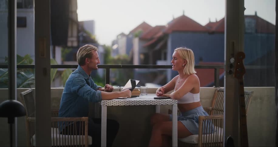 Two people sitting at a table on the porch talking