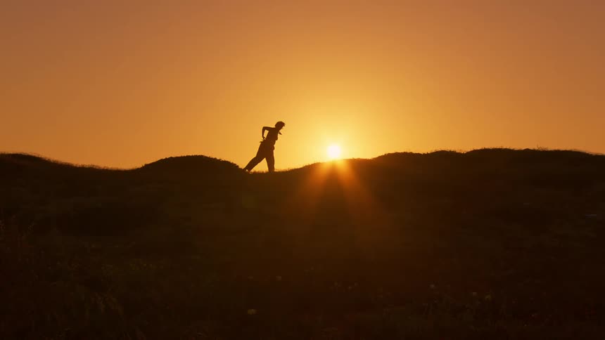 A silhouette of a person doing martial movements against the orange sky and strong sunlight