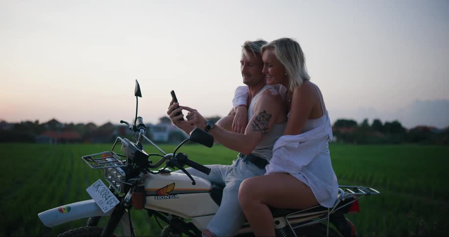 A woman laughs while holding on to a man on a motorcycle