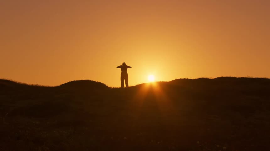 Silhouette of a person on a hill against a setting sun