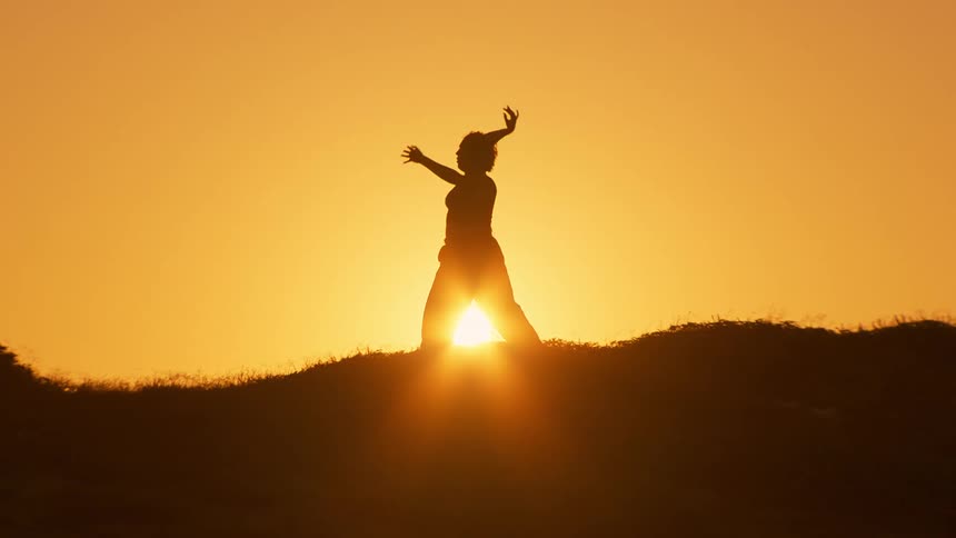 A woman stretches on a grassy area with the sun behind her