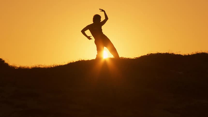 Woman silhouetted by the setting sun slowly moves through multiple poses
