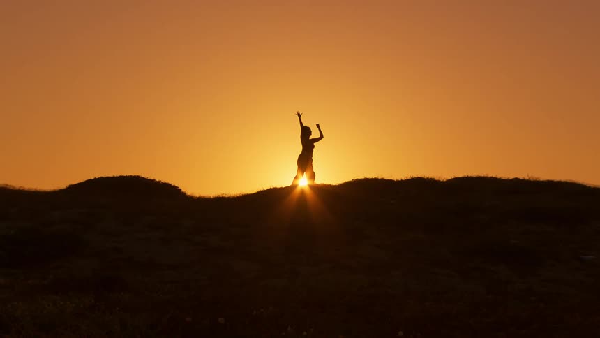 A individual dances on a hill silhouetted by the setting sun