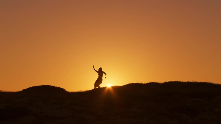 A woman dancing on a hills ridge at sunrise