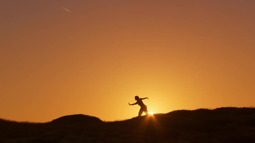 An individual doing yoga poses silhouetted by the setting or rising sun