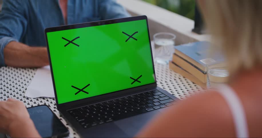 A blonde person looking at a laptop with a green screen and black xs in the corners