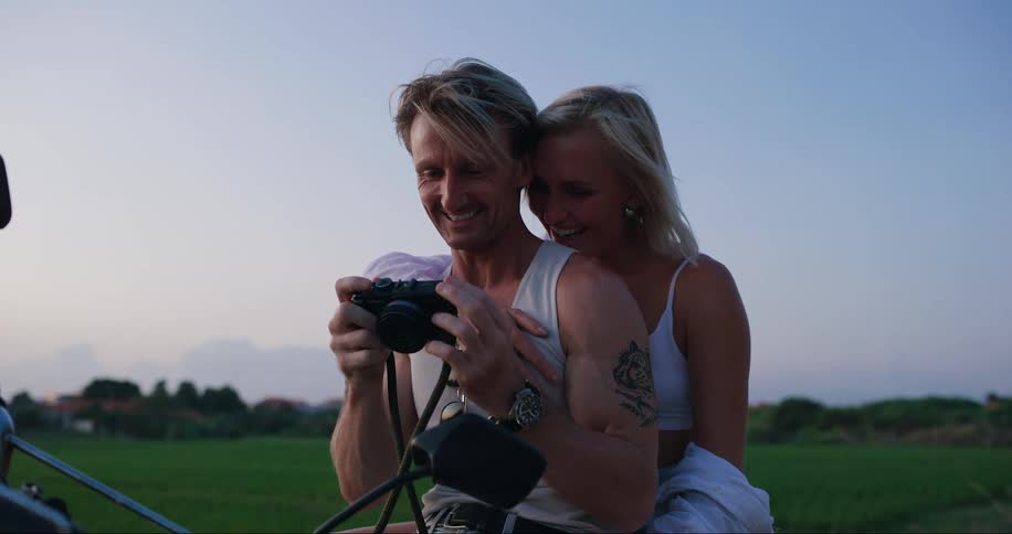 A man is showing a camera to the woman who is behind him or hugging and they are both happy and smiling