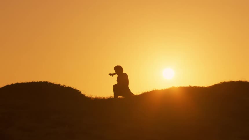 Silhouette of a person dancing on a hill against a golden sun