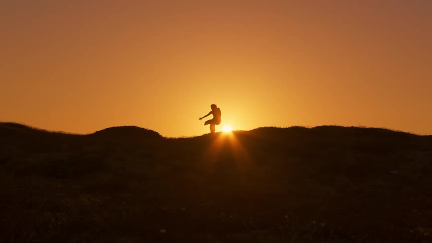 A silhouette of a woman dancing over a hill against the backdrop of a setting sun