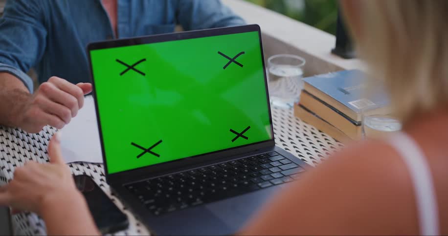 A woman uses a laptop with a green screen and placeholder markings on its display placed on a table