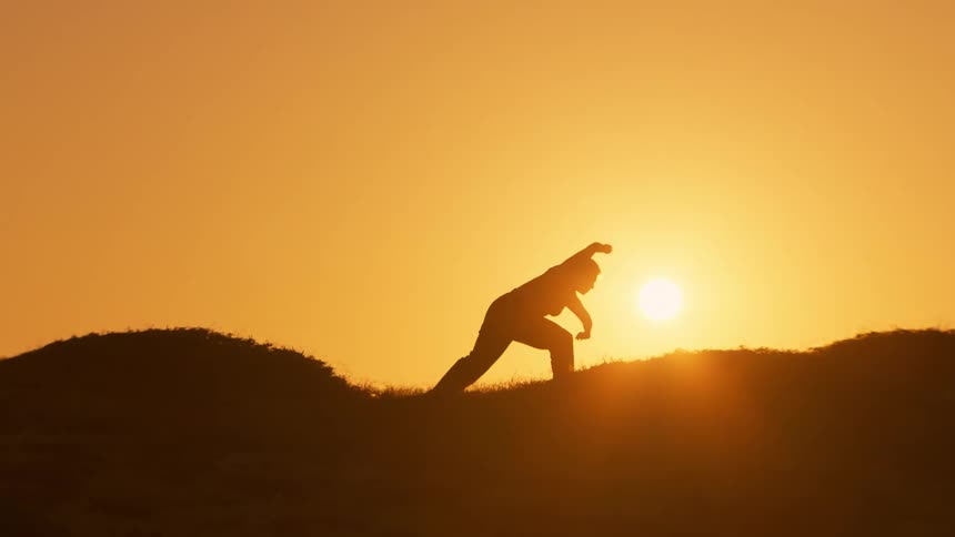 A woman in silhouette stretching on a grassy area at dusk