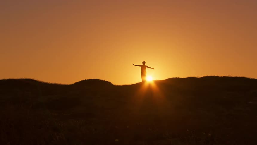 Person in silhouette dances on mountain sunrise