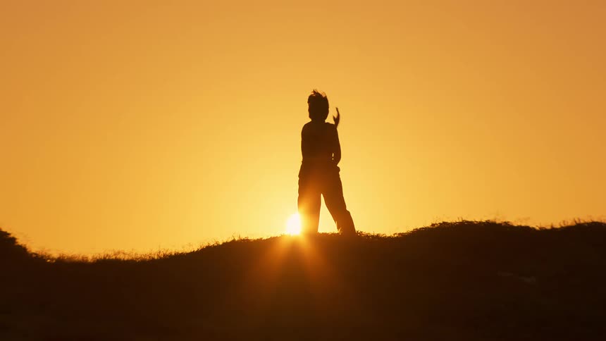 Person dances on hill in silhouette sunrise