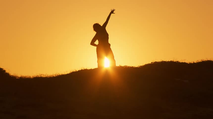 Silhouette of a person exercising on a hill against a golden sun