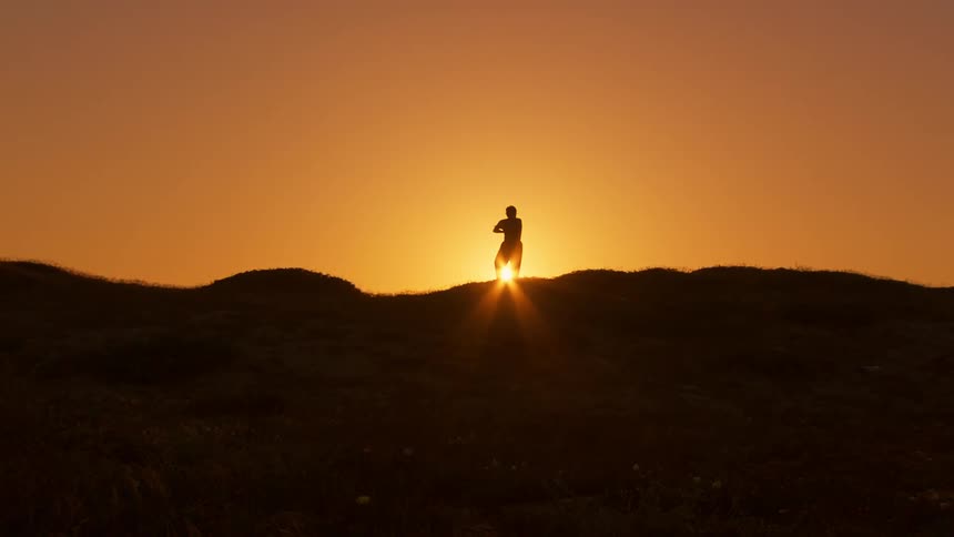 Silhouette of a person doing tai chi while standing on a hill against the orange sky