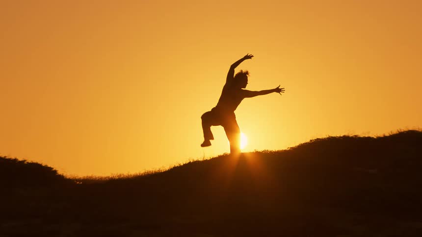 Silhouette of a person on a mountain peak against the setting sun dancing