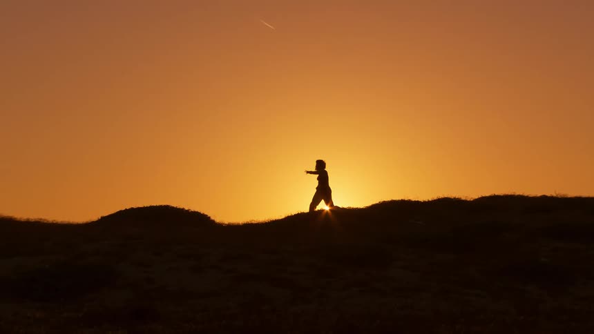 Person in silhouette dances on hillside at sunrise