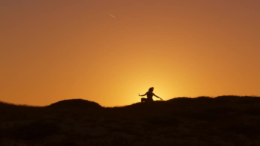 Woman silhouetted against orange sky after sunset moves through various poses