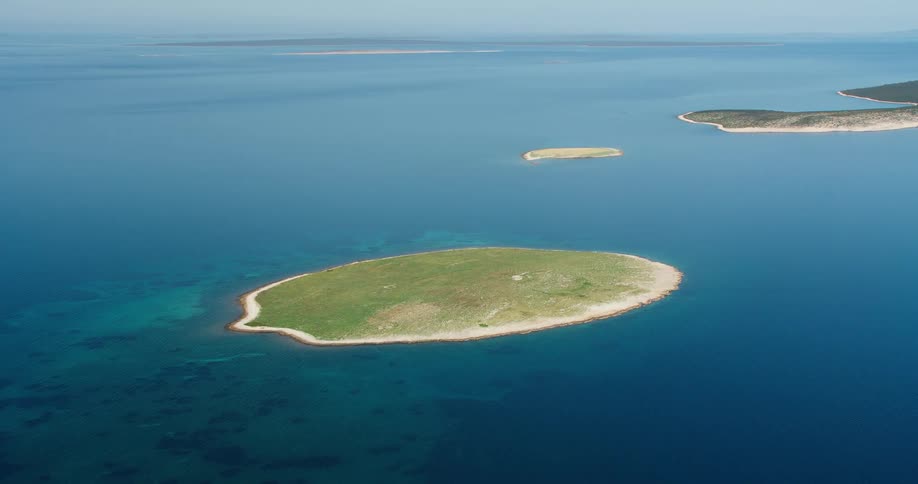 An aerial view of a small island in the middle of the blue sea and there are some other islands further away