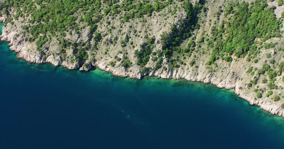An aerial view of a rugged coastline with steep cliffs descending into clear blue waters
