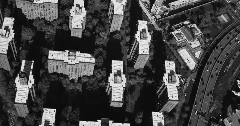 An aerial view in black and white of several identical condominiums and there are many trees in the region