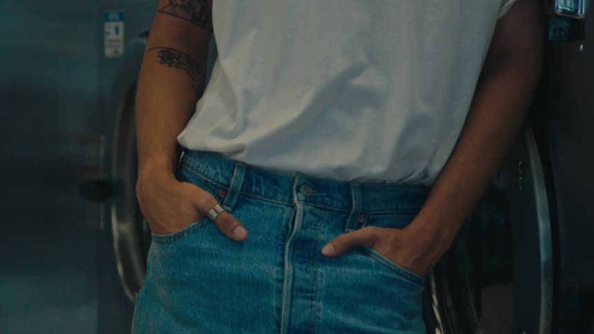 Closeup of a persons waist with their hands in the pockets of their jeans next to the washing machine