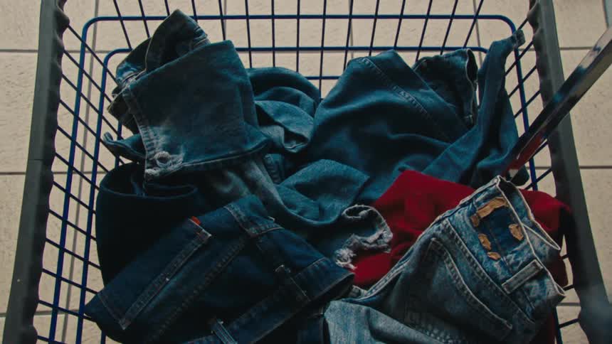 Supermarket cart with denim clothes and a hand picking up