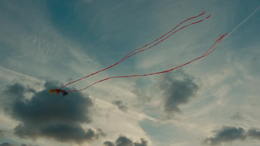 A kite is flying high in the cloudy sky