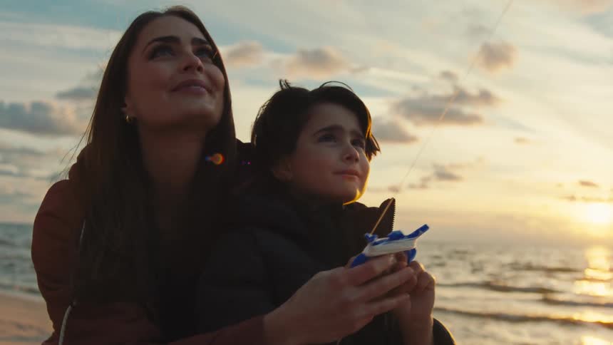 Mother and son playing with toy that releases water while on the beach at sunset