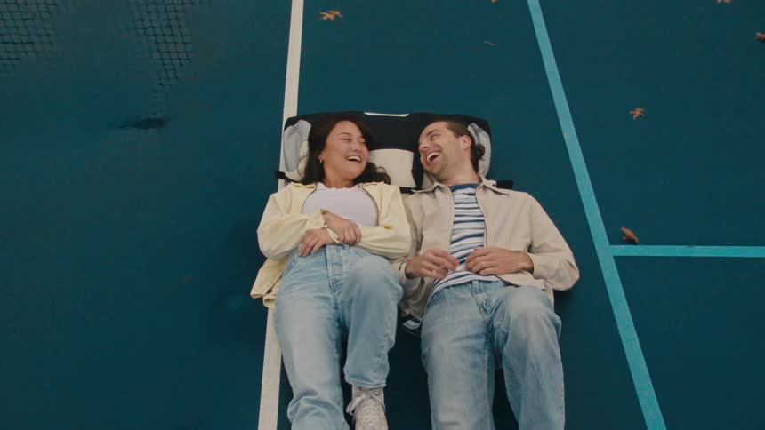 Man and woman lying side by side on a tennis court