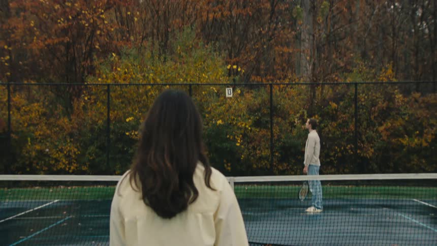 Man and woman playing tennis on a wet court with trees in the background