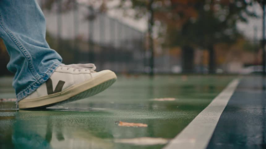 Man wearing jeans and white sneakers bounces a tennis ballon a wet outdoor tennis court