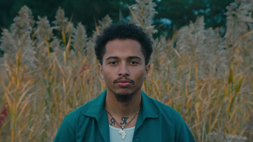 Man stands in a field next to tall plants waving in the wind